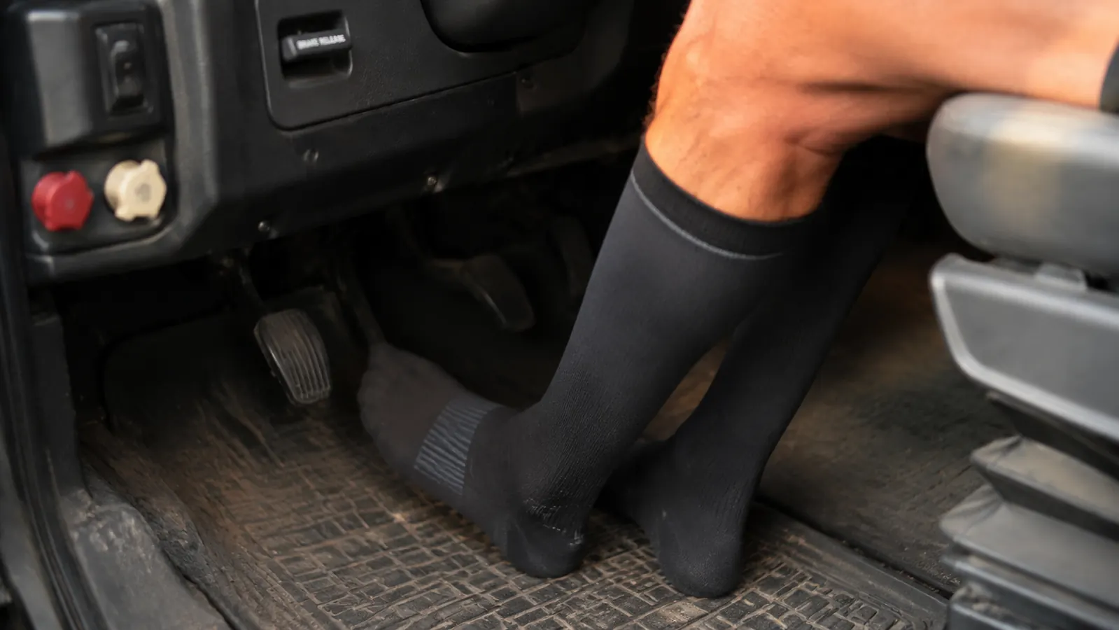 Driver's lower legs in dark compression socks visible beneath a truck cab dashboard during a long haul